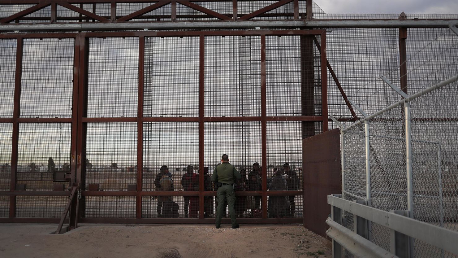 In this February 1, 2019, file photo, a US Border Patrol agent speaks with Central American immigrants at the US-Mexico border fence in El Paso, Texas. 