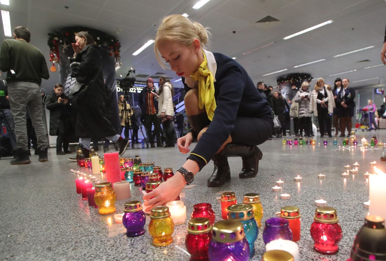 A Ukraine International Airlines employee lights a candle that is part of a symbolic runway at the airport memorial.