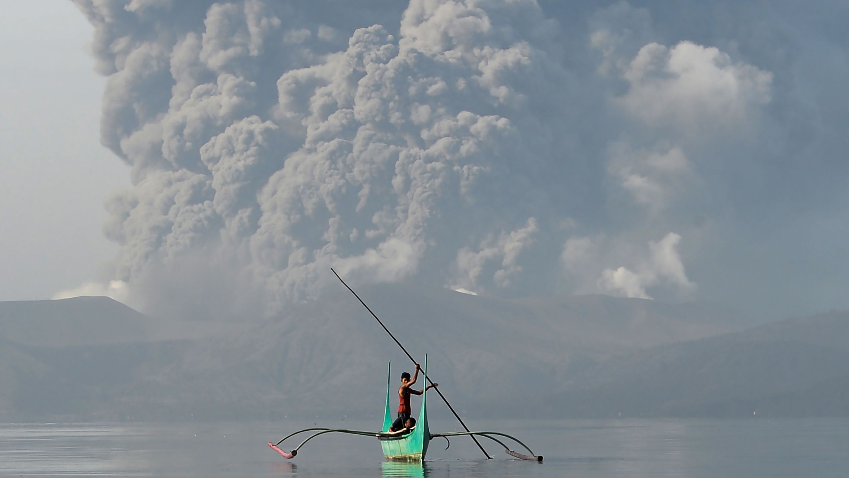 A youth rides an outrigger canoe while the volcano spews ash on January 13.
