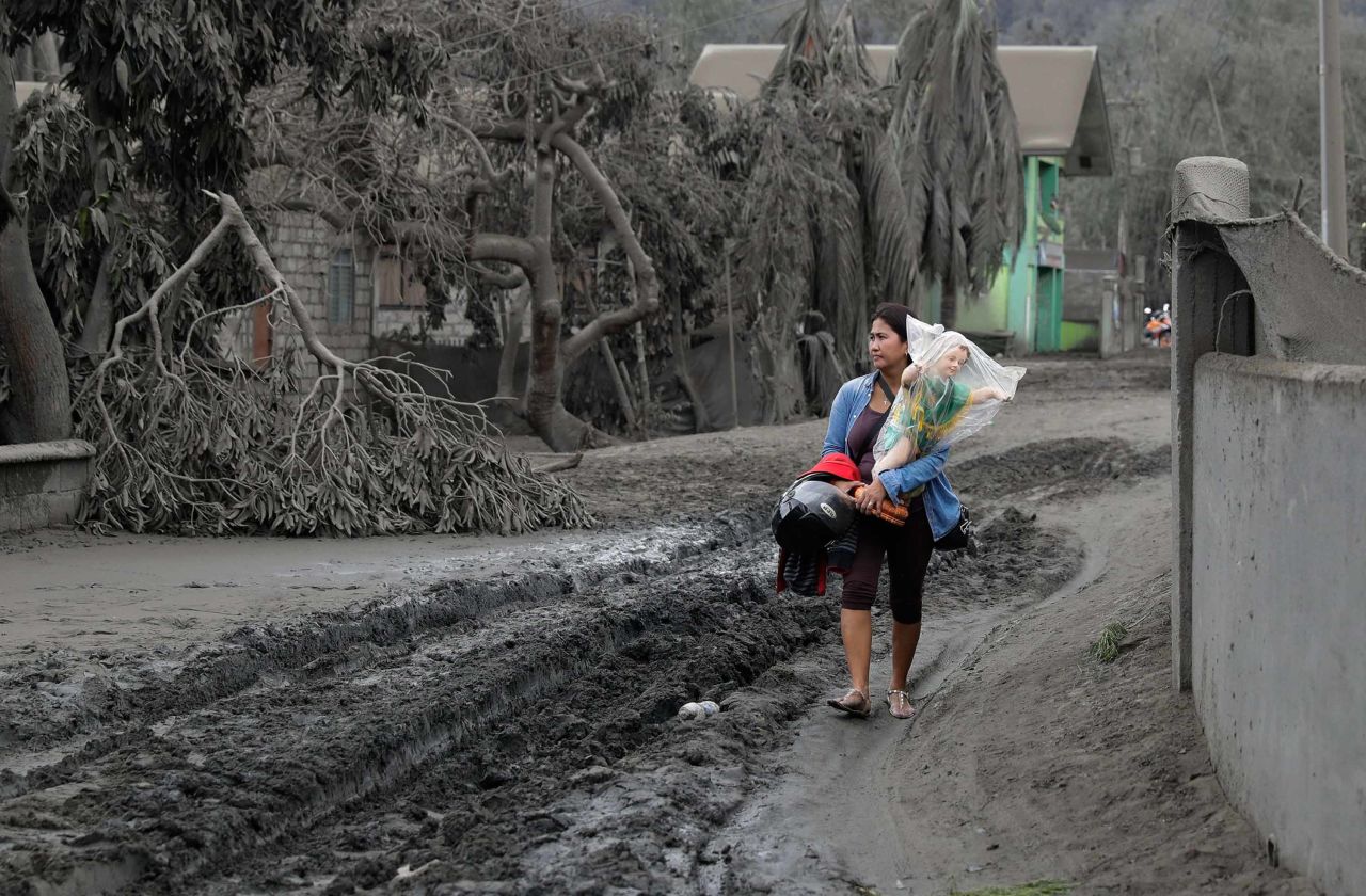 Leila de Castro carries a religious statue recovered from a family member's house as she walks along an ash-covered road in Boso-Boso on January 14.