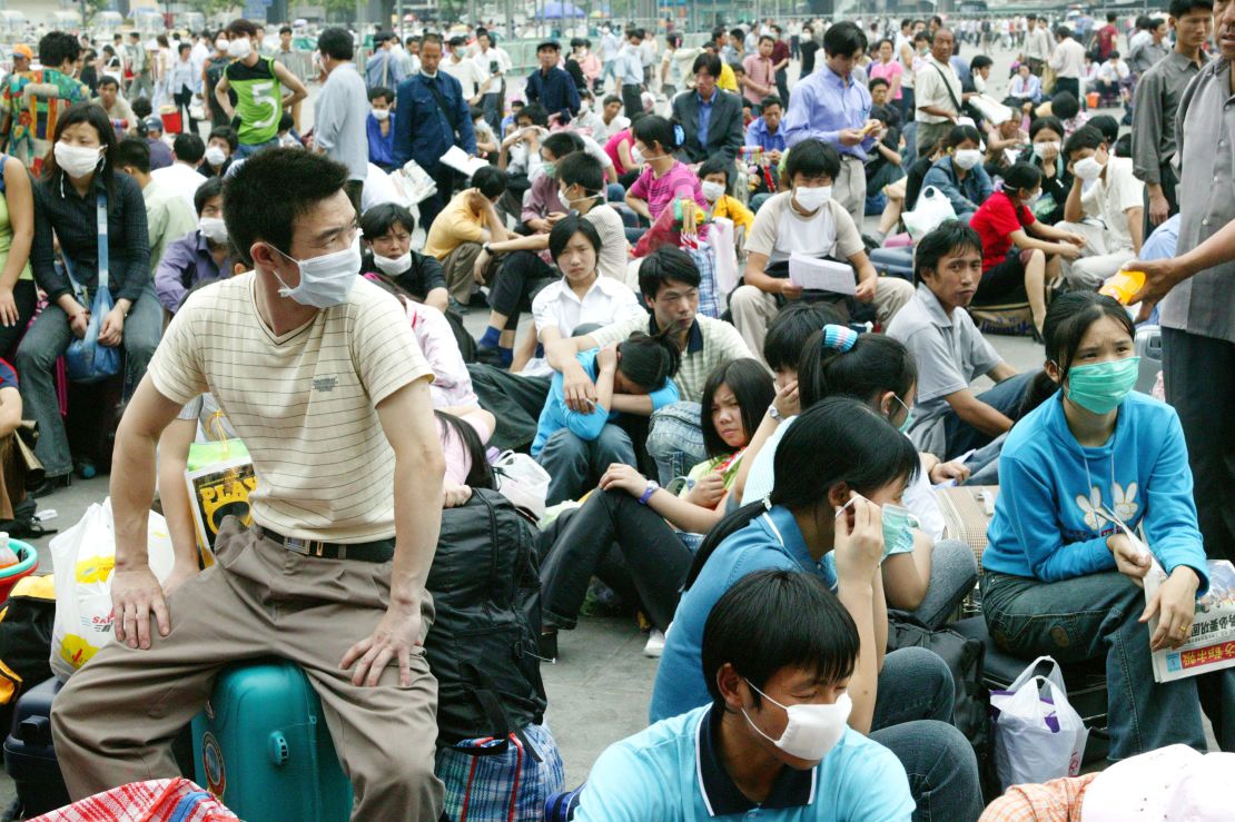 Migrant workers in face masks wait outside the train station in Guangzhou, China, before returning home during the SARS outbreak in 2003.