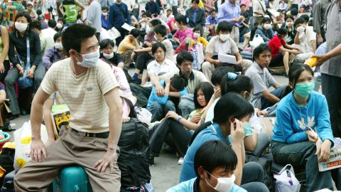 Migrant workers in face masks wait outside the train station in Guangzhou, China, before returning home during the SARS outbreak in 2003.