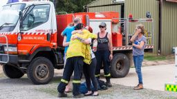 COOMA, AUSTRALIA - JANUARY 23: People are seen embracing at Numeralla Rural Fire Brigade near the scene of a water tanker plane crash on January 23, 2020 in Cooma, Australia. Three American firefighters have have died after their C-130 water tanker plane crashed while battling a bushfire near Cooma in southern NSW this afternoon. The repurposed C-130 Hercules, built in America by Lockheed Martin, took off from Richmond RAAF base at 1pm, and disappeared from the flight radar just after 2pm. Coulson Aviation, the Canadian operator of the C-130 aircraft, has now grounded their fleet as a mark of respect for the victims and to re-assess safety conditions. Hot and windy conditions have seen a number of fires flare up across southern NSW this afternoon, with firefighters battling numerous blazes in temperatures over 40 degrees Celsius in some parts. (Photo by Jenny Evans/Getty Images)