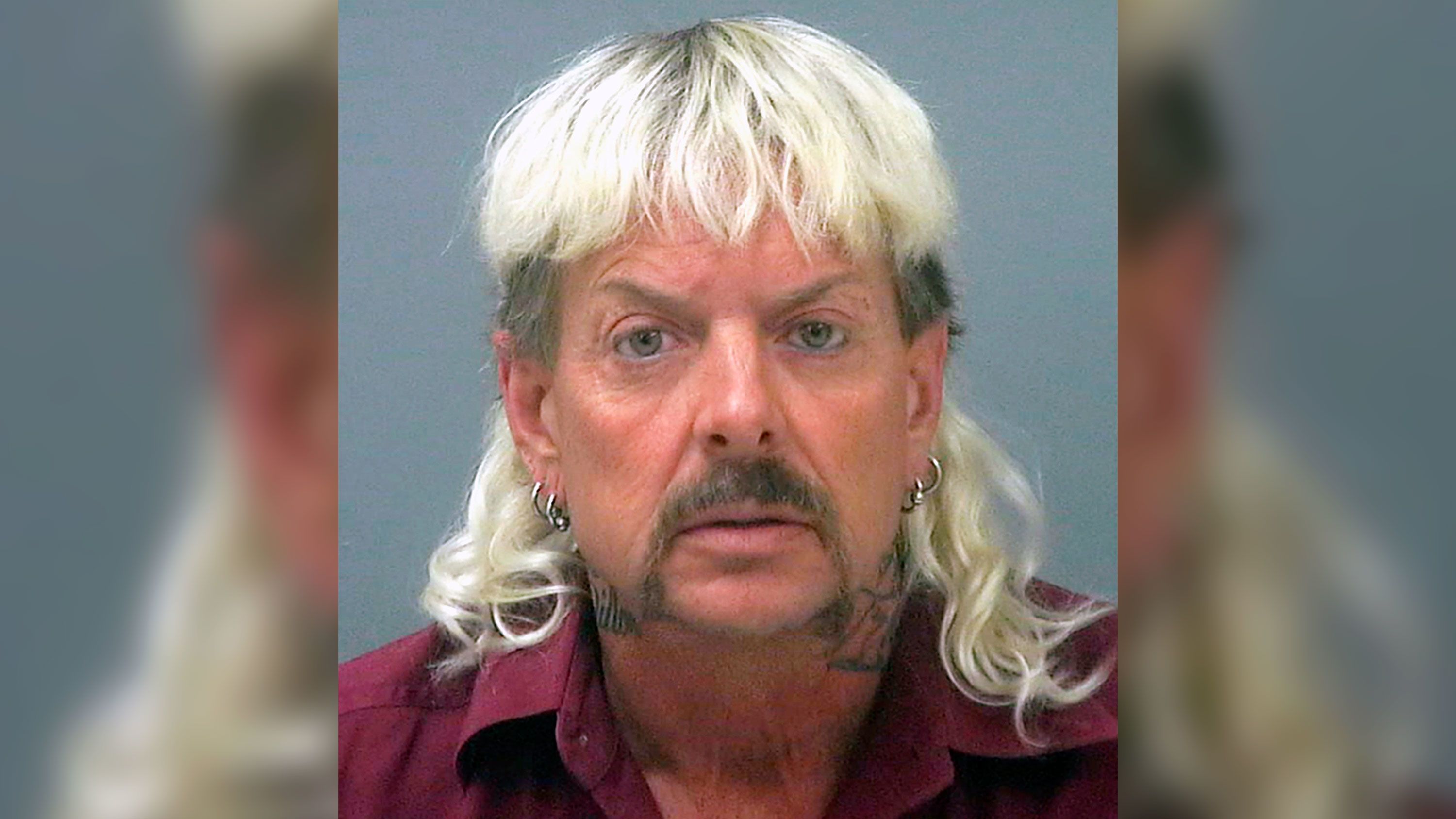 Joe Exotic’s mugshot shows him with a platinum blond mullet, maroon shirt, hoop earrings, and a serious expression following his arrest and conviction.