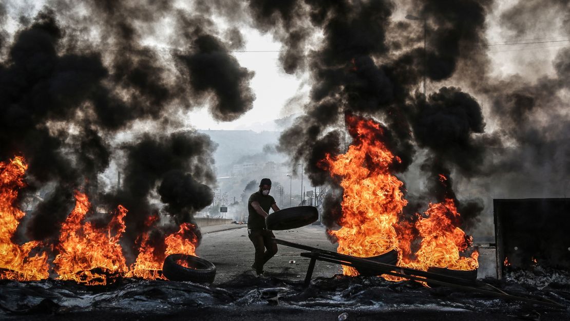 A Lebanese man throws a tyre on a burning barricade during an anti-government protest on October 17, 2019.