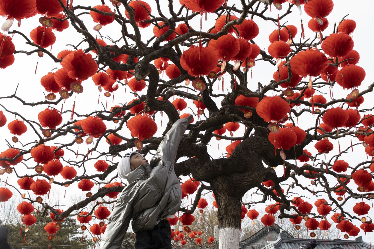 A child jumps to touch lanterns hung on a tree in Beijing on Thursday, January 16.