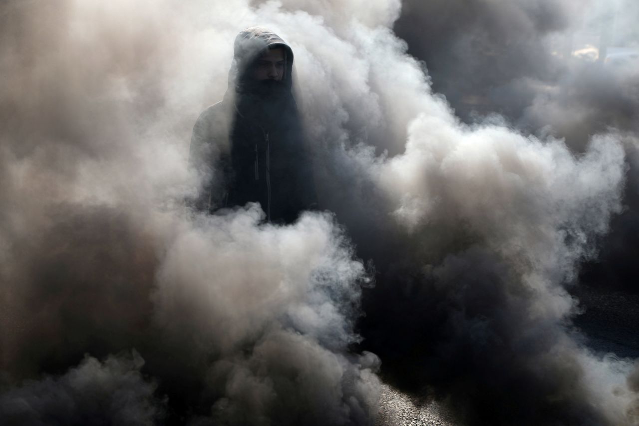 A demonstrator walks among smoke from burning tires during ongoing anti-government protests in Kerbala, Iraq, on Monday, January 20.