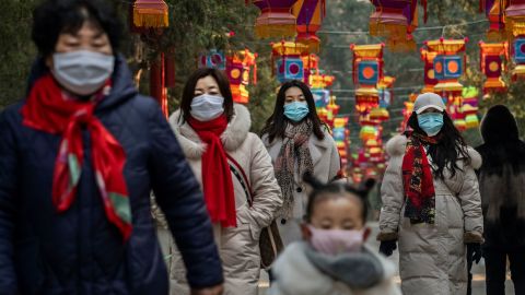 Chinese women and children wear protective masks as they walk under decorations in a park after celebrations for the Chinese New Year and Spring Festival were cancelled by authorities on January 25, 2020 in Beijing, China. 