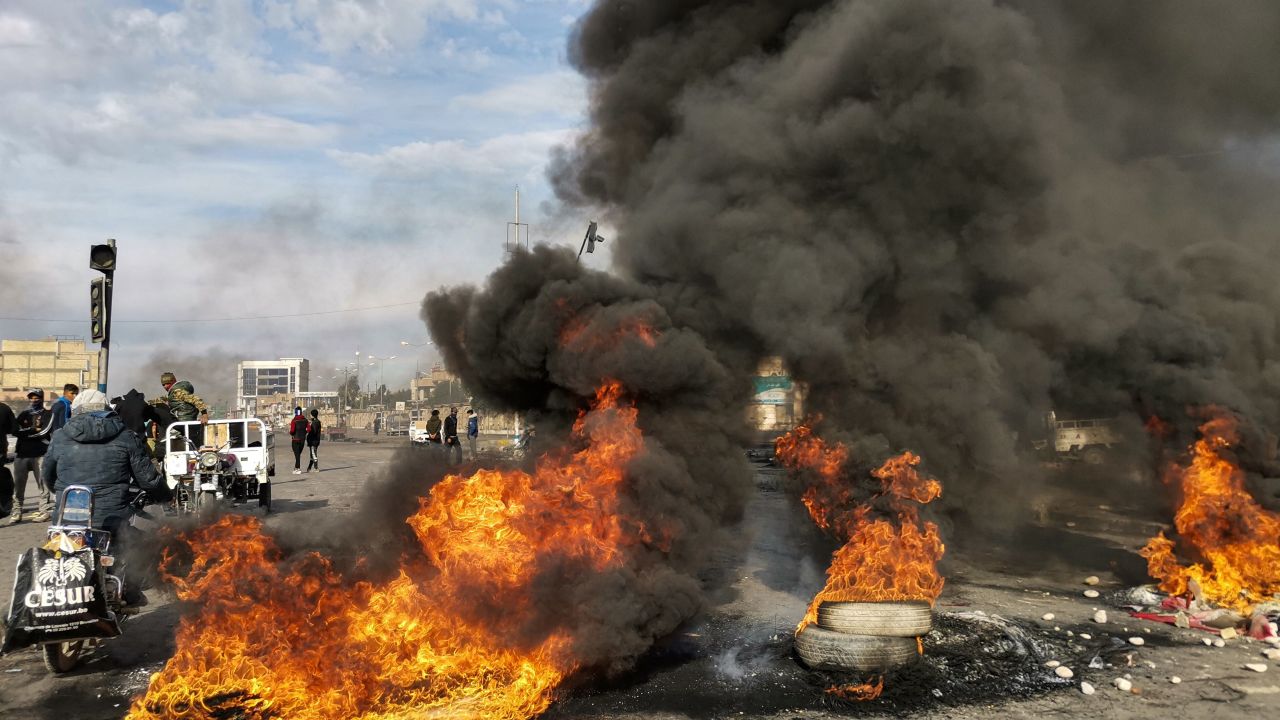 Protesters stand by burning tires at a makeshift roadblock in the city of Nasiriyah on Saturday.