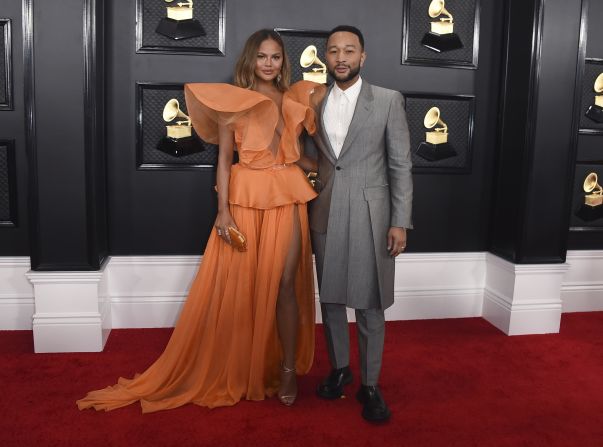 Chrissy Teigen and John Legend arrive at the Grammy Awards. Teigen wore an orange Yanina Couture gown with elaborate sleeves while Legend sported a long gray tailored suit. 