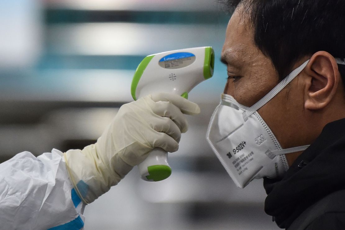 A medical staff member takes the temperature of a man at the Wuhan Red Cross Hospital in Wuhan on January 25, 2020.