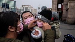 A mother (L) of a child (R) held by his father (C) adjust his protective mask to help stop the spread of a deadly virus which began in Wuhan peaks through a plastic curtain at the Beijing railway station in Beijing on January 27, 2020. - China on January 27 extended its biggest national holiday to buy time in the fight against a viral epidemic and neighbouring Mongolia closed its border, after the death toll spiked to 81 despite unprecedented quarantine measures. (Photo by NICOLAS ASFOURI / AFP) (Photo by NICOLAS ASFOURI/AFP via Getty Images)