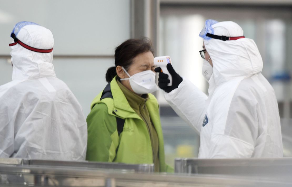 An official checks the temperature of a passenger in front of a train ticket gate at Beijing international airport on January 27, 2020, amid the outbreak of a novel coronavirus.