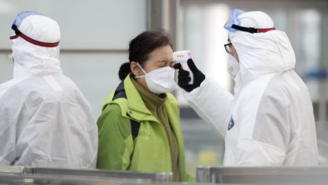 An official checks the temperature of a passenger in front of a train ticket gate at Beijing international airport on January 27, 2020, amid the outbreak of a novel coronavirus. 