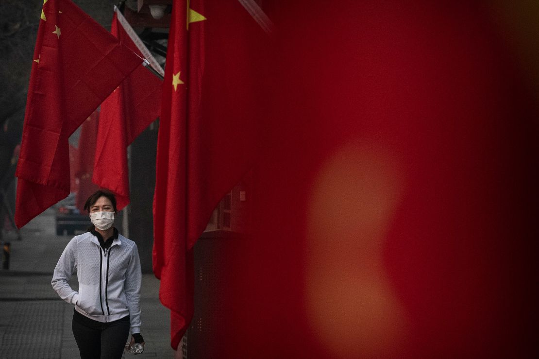 A woman wears a protective mask as she walks by Chinese flags in Beijing during the Lunar New Year holiday.