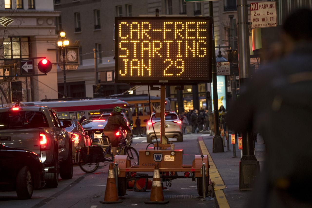 Vehicles drive past a "Car-Free" sign displayed on Montgomery Street in San Francisco, California.