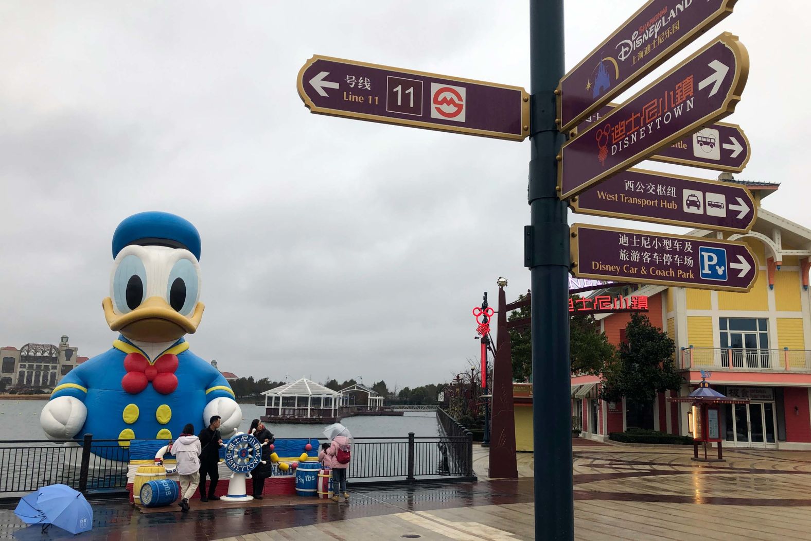 Visitors carry umbrellas as they walk through the Disneytown area of the Shanghai Disney Resort, which announced that it will be closed indefinitely from January 25, as the virus continues to spread.