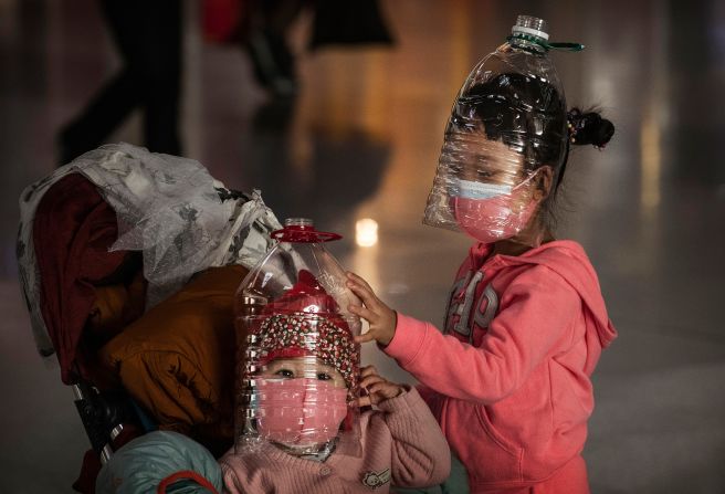 Children wear plastic bottles as makeshift masks while waiting to check in to a flight at the Beijing Capital Airport on January 30, 2020.
