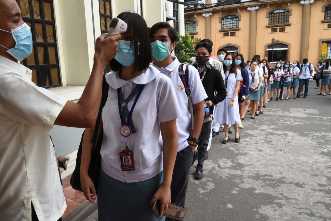Students wearing protective face masks have their temperatures taken while entering their college campus in Manila.