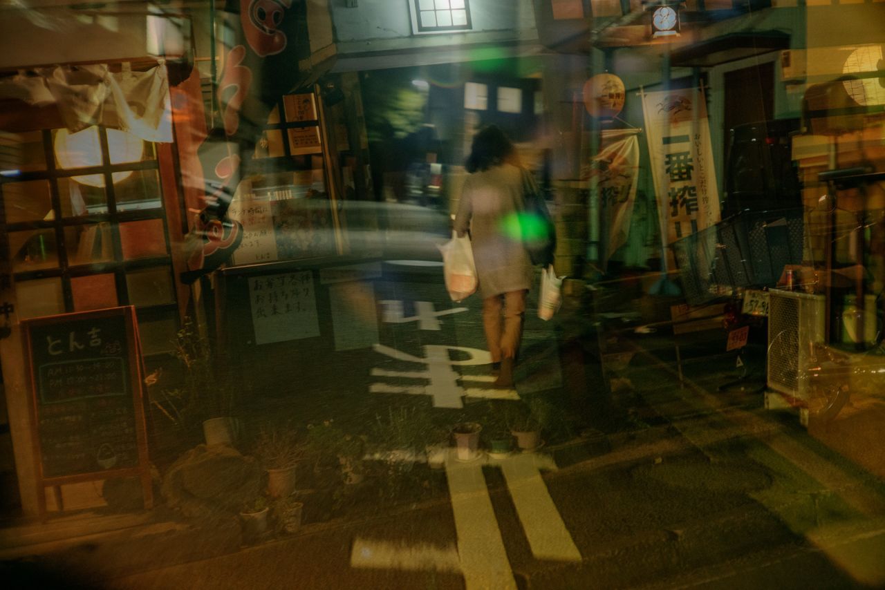 A woman walks in a residential area in Yokohama as the city's bright lights shine over her.