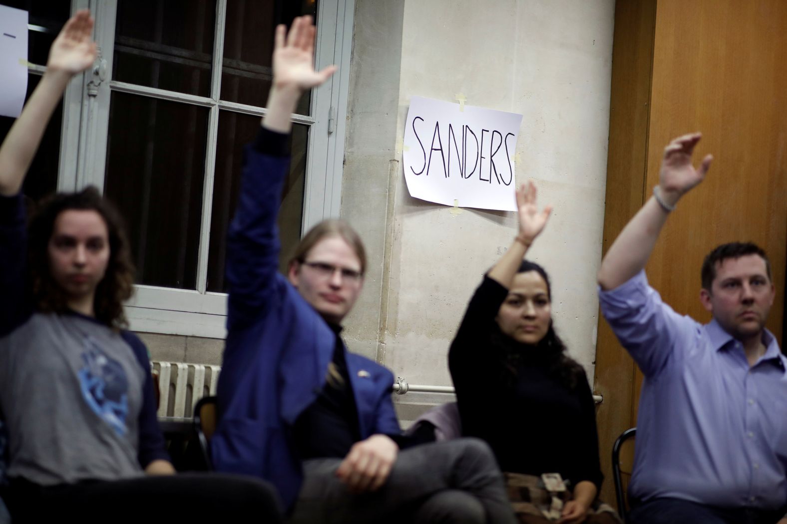 Iowa voters in Paris raise their hand as they gather to caucus.