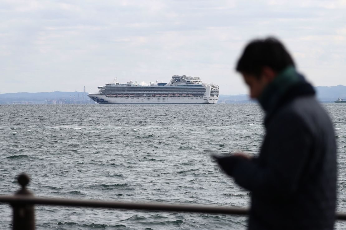 A member of the media checks his phone as the Diamond Princess cruise ship sits anchored in quarantine off the port of Yokohama on Tuesday.