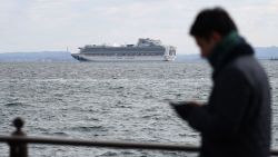 A member of the media checks his phone as the Diamond Princess cruise ship with over 3,000 people sits anchored in quarantine off the port of Yokohama on February 4, 2020, a day after it arrived with passengers feeling ill. - Japan has quarantined the cruise ship carrying 3,711 people and was testing those onboard for the new coronavirus on February 4 after a passenger who departed in Hong Kong tested positive for the virus