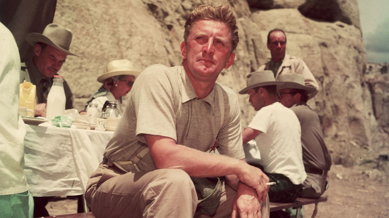 1951: American actor Kirk Douglas sits at a picnic table on the desert location for director Billy Wilder's film, 'Ace In The Hole.'