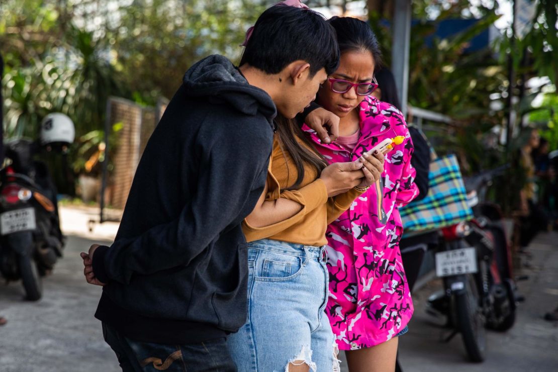 Thai people check the news on a phone near the shopping mall where a mass shooting took place on Saturday in Korat.