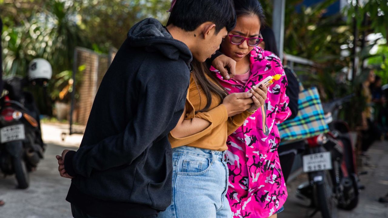 Thai people check the news on a phone near the shopping mall where a mass shooting took place on Saturday in Korat.