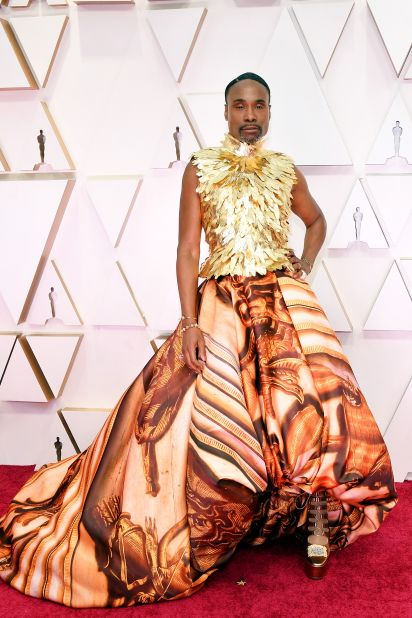 Billy Porter looks like royalty in a glistening gold gown featuring a sleeveless bodice with gold feathers and a floor-length skirt in a rich baroque-style print. The ensemble was inspired by Kensington Palace and designed by British designer Giles Deacon.