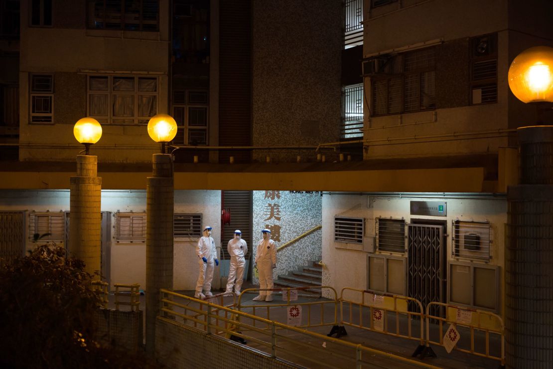 Officials wearing protective gear stand guard outside an entrance to the Hong Mei House residential building.