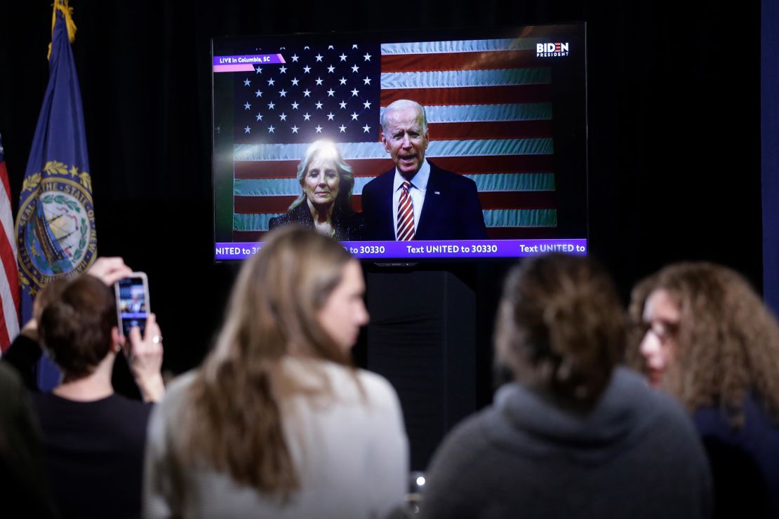 Supporters of Democratic presidential candidate former Vice President Joe Biden watch as Biden, behind right, and his wife Jill Biden, behind left, appear in a video transmission during a primary election night rally.