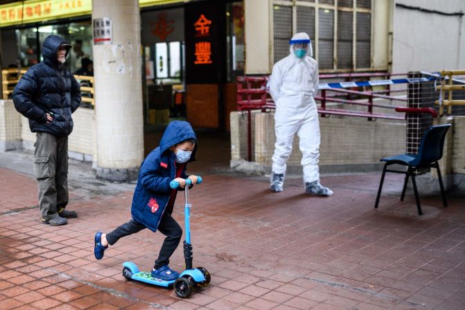A child rides a scooter past a police officer wearing protective gear outside the Hong Mei House in Hong Kong. More than 100 people evacuated the housing block after four residents in two different apartments tested positive for the coronavirus.