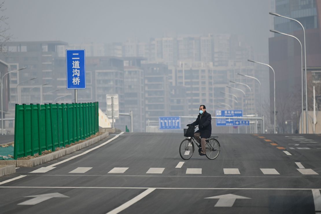 A man wearing a face mask rides his bicycle along an empty street in Beijing on February 12, 2020.