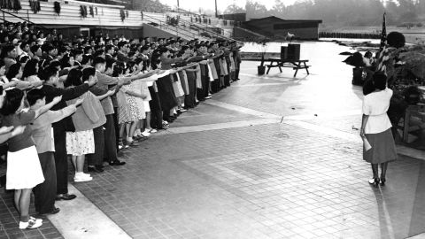 A group of Japanese American high school student say the Pledge of Allegiance before their graduation ceremony. Shortly afterwards, they will be sent to a relocation camp. Santa Anita, California, June 1942. 