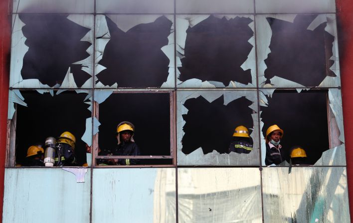 Firefighters in Yangon, Myanmar, stand near broken windows while rescuing people from a fire that broke out at a 12-story building on Thursday, February 20.
