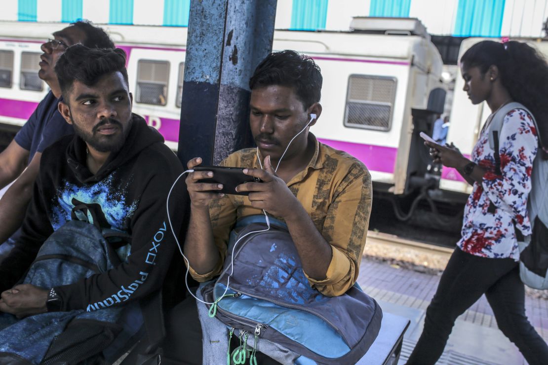 Passengers use smartphones while sitting on a platform of a railway station in Mumbai, India, on Saturday, Feb. 15, 2020. 