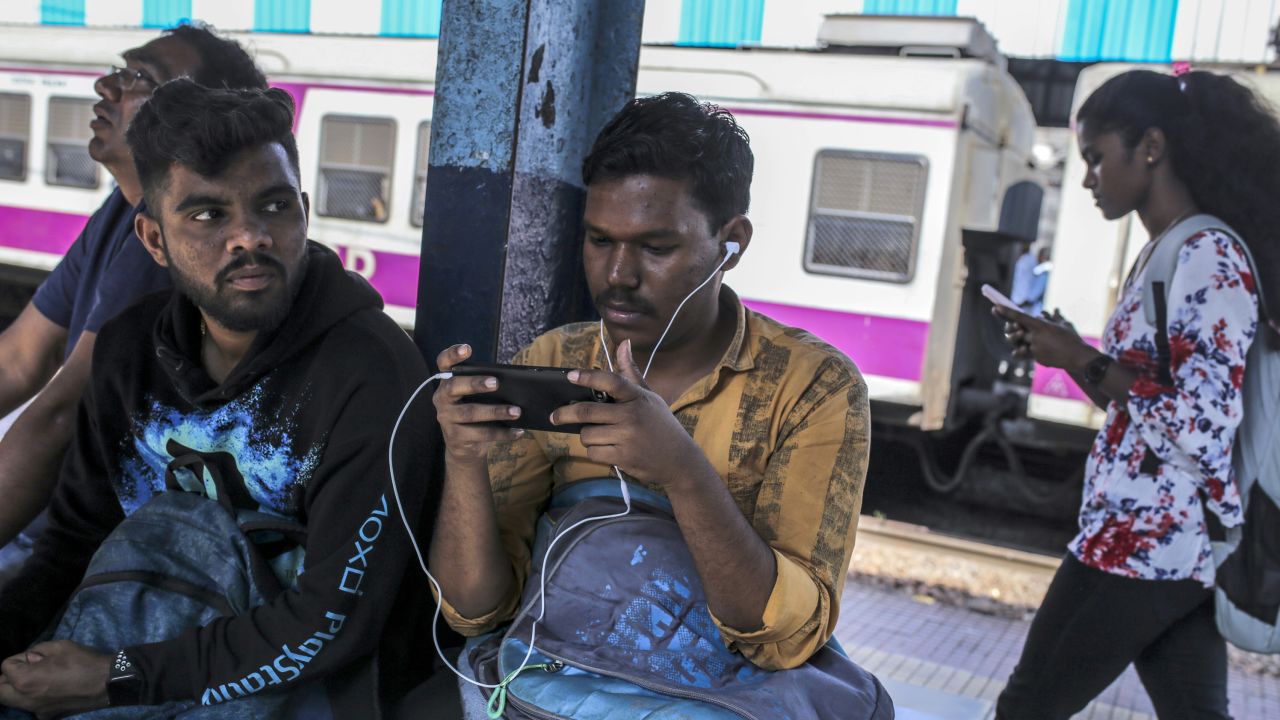 Passengers use smartphones while sitting on a platform of a railway station in Mumbai, India, on Saturday, Feb. 15, 2020. 