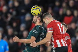 John Egan (12) of Sheffield United challenges Andy Carroll (7) of Newcastle United for the ball in an English Premier League game.
