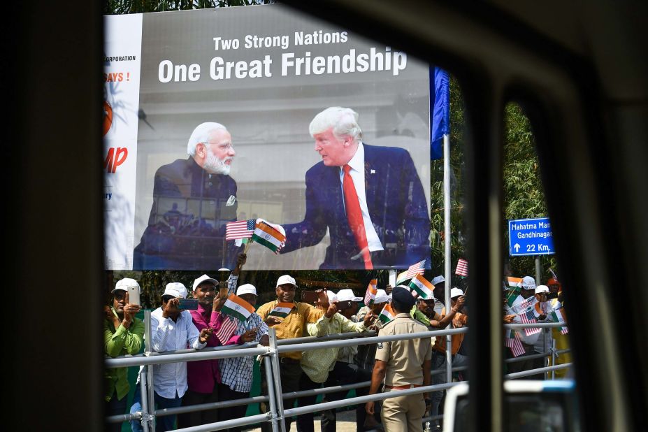 People wave flags as Trump's motorcade drives past them in Ahmedabad.