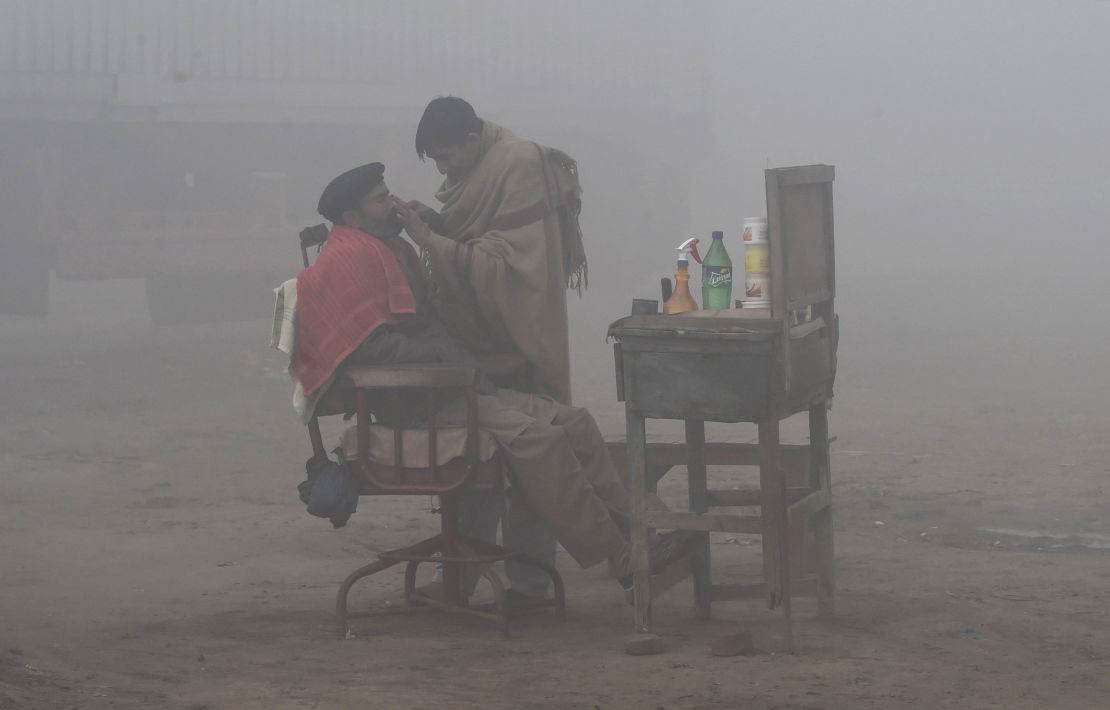  A Pakistani barber shaves a customer alongside a road amid heavy fog and smog conditions in Lahore.
