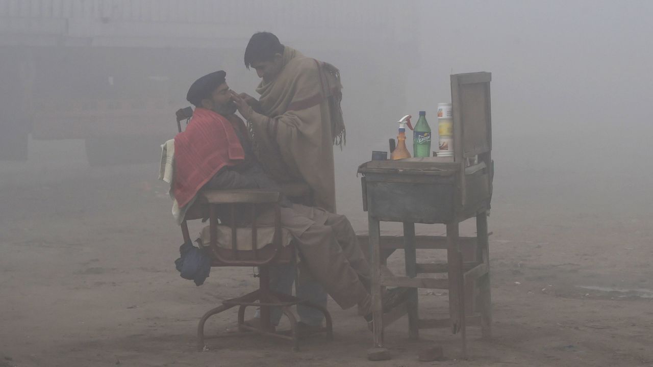  A Pakistani barber shaves a customer alongside a road amid heavy fog and smog conditions in Lahore.