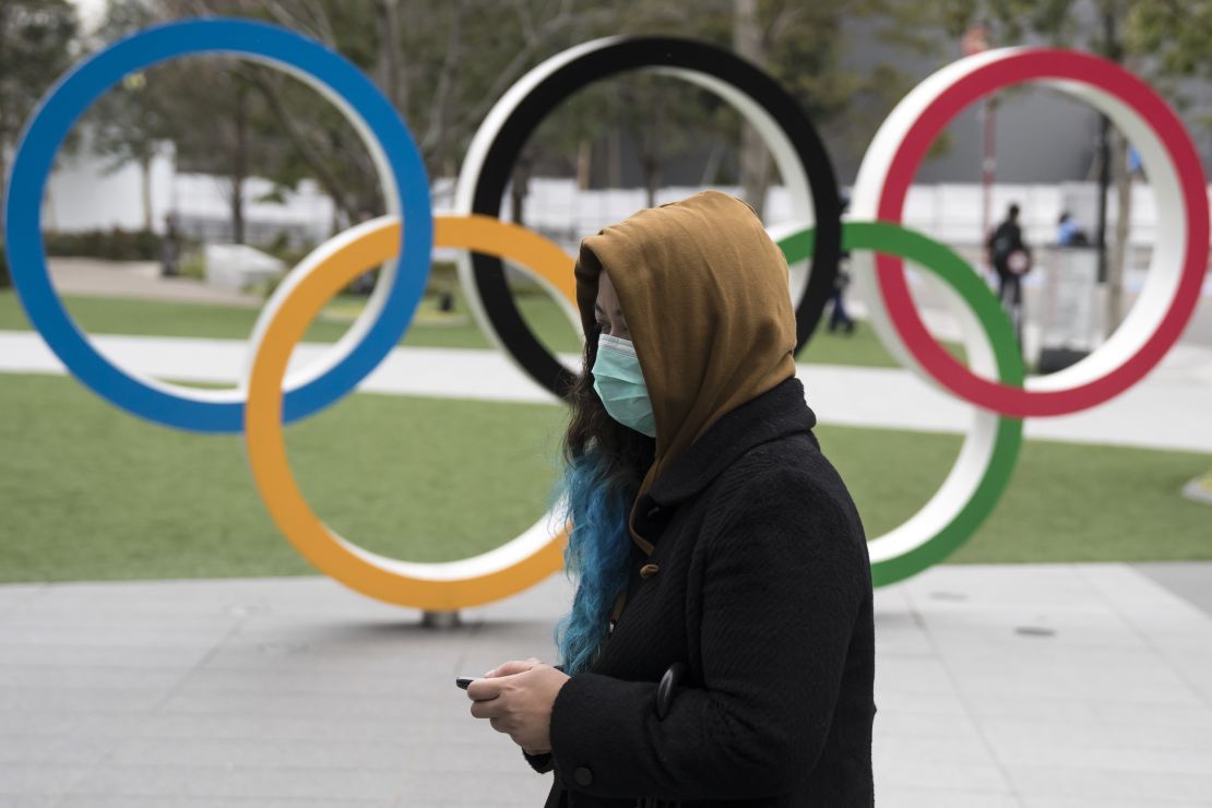 A woman wearing a face mask walks past the Olympic rings in front of the new National Stadium, the main stadium for Tokyo 2020.