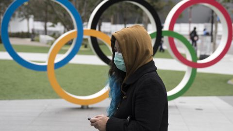 A woman wearing a face mask walks past the Olympic rings in front of the new National Stadium, the main stadium for Tokyo 2020.