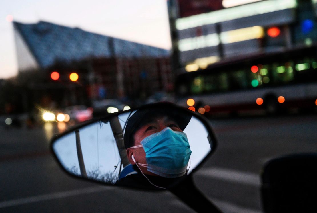 A Chinese man is seen in the side mirror of his scooter as he wears a protective mask while waiting at a red light in Beijing.