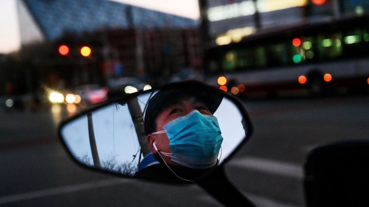 A Chinese man is seen in the side mirror of his scooter as he wears a protective mask while waiting at a red light in Beijing.