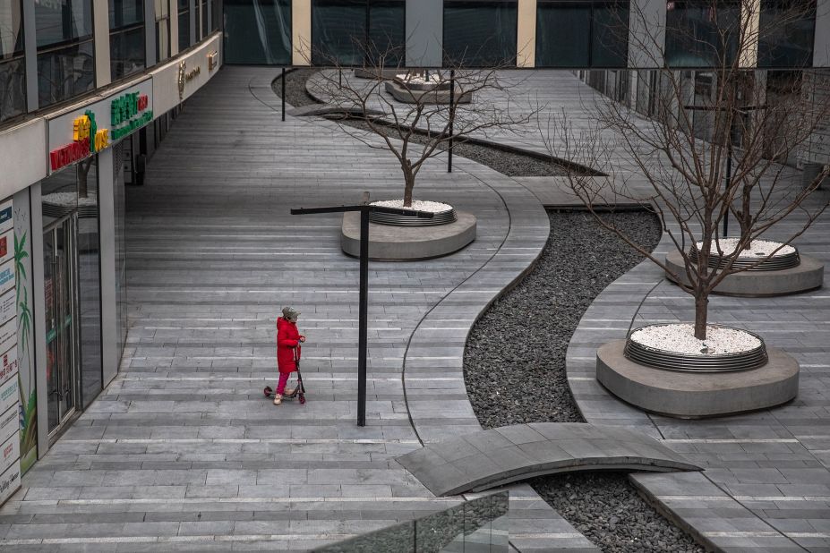 A child wearing a protective face mask rides on a scooter in an empty area in Beijing.