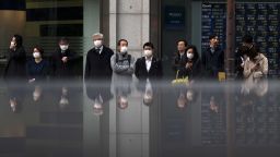 Pedestrians wearing face masks wait to cross a road in front of a monitor displaying stock information outside a securities firm on February 25 in Tokyo, Japan. 