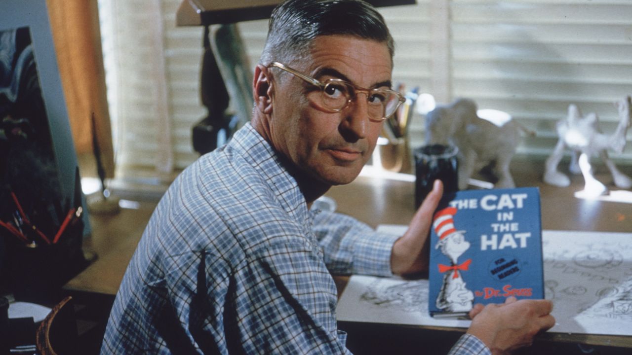 American author and illustrator Dr Seuss (Theodor Seuss Geisel, 1904 - 1991) sits at his drafting table in his home office with a copy of his book, 'The Cat in the Hat'.